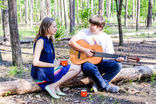 Portrait Of Young Loving Happy Couple With Guitar In Forest. Cute Girl And Man Singing Playing Acoustic Guitar In Forest Having Fun.