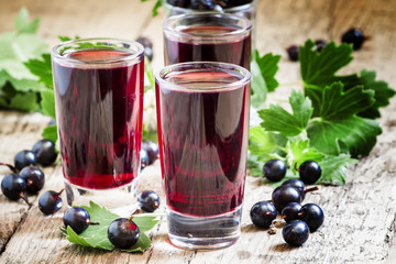 Fresh black currant juice with berries in glasses on an old wood