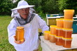 pszczelarz w pasiece prezentujący słoik świeżego miodu