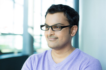 Wall Mural - Closeup headshot portrait, happy handsome businessman, wearing black glasses, looking sideways, isolated inside office background.