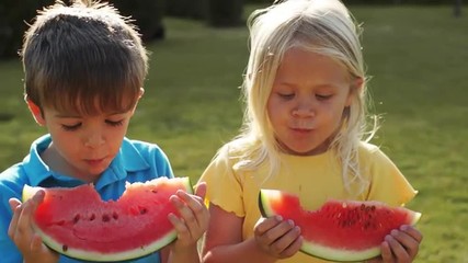 two children eating water melon in park.