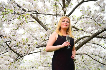 Beautiful female with glass of champagne in the sakura garden