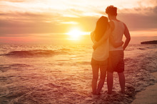 Young Couple Watching Sunset On The Beach