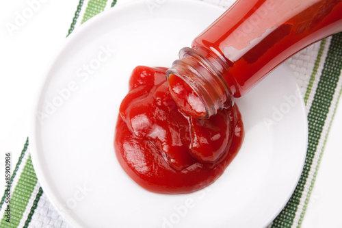 Fotografía Pouring Ketchup from the Bottle – Ketchup pours from the bottle onto a white plate