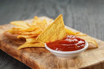 tortilla chips on olive board with tomato sauce, on wooden table