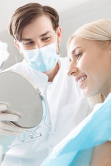 Wall Mural - Smiling woman looking in mirror by dentist