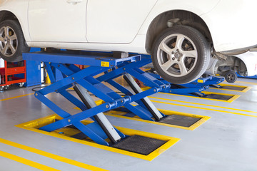 jacks lift white car up for wheel tire replacement in garage