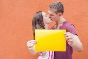 Wall Mural - Young couple kissing and holding frame at background of wall