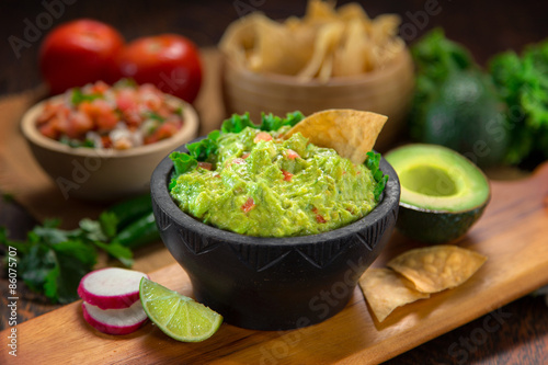 Fotografie, Obraz Lahodné Mísa guacamole vedle čerstvých surovin na stůl s tortilla chipsy a salsa