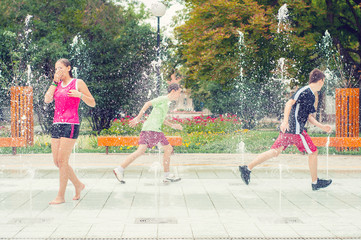 Wall Mural - Teenage boys and girls having fun in the towns water fountain on