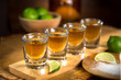 Four shot glasses with tequila bottle and bowl of limes with salt at a bar