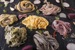 Raw fresh pasta tagliatelle in six color decor with herbs on black stone