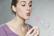 gorgeous young woman with purple sweater blowing bubbles on neutral background