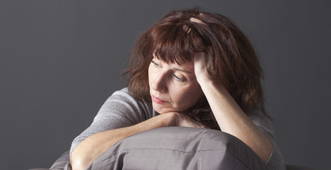 tired mature woman resting her face and hands laying down on cushions for comfort while having health care problems