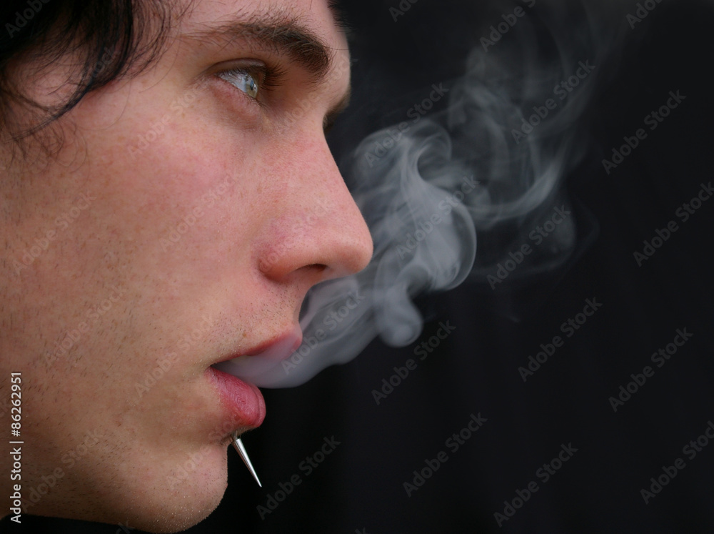 A man with a piercing blowing cigarette smoke out his mouth Stock Photo