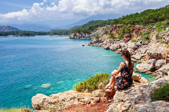 Tourist girl sitting and looking on bay of old greek town Phaselis. Panoramic view on coast near Kemer, Antalya, Turkey.