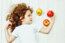 Happy Child With Red Apples On Light Wooden Floor. Top View.