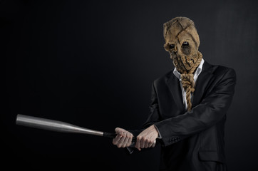 Fear and Halloween theme: a brutal killer in a mask holding a bat on a dark background in the studio