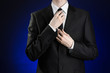 © Alex - Businessman and gesture topic: a man in a black suit and white shirt correcting a jacket and tie on a dark blue background in studio isolated