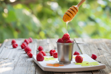 Raspberry in a cup with flowing honey from a dizzler, on wood ta