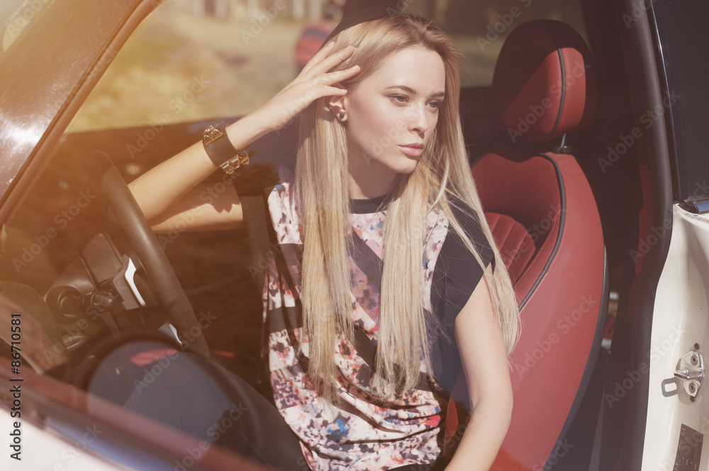 Nice portrait of blonde young woman at the wheel of sport car with red interior, with sunglasses - obrazy, fototapety, plakaty 