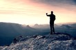 Tall hiker is taking photo by smart phone on the peak of mountain  at sunrise.
