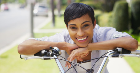 African woman smiling and leaning on bicycle handlebars