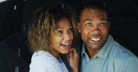 Black couple laughing under umbrella together