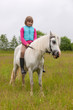 Young girl child sitting astride a white horse and smiling  Outdoors