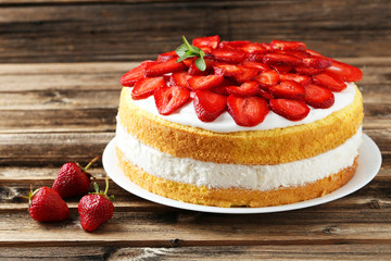 Sweet cake with strawberries on plate on brown wooden background