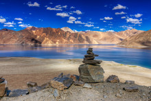 Rocks And Reflection Of Mountains On Pangong Tso (Lake) With Blue Sky. It Is Huge Lake In Ladakh, It Is 134 Km Long And Extends From India To Tibet. Leh, Ladakh, Jammu And Kashmir, India