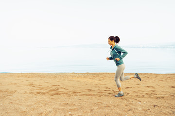 Canvas Print - Sporty young woman running on sand beach