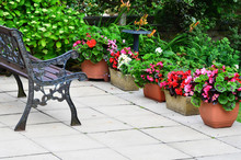 Colorful English Patio Area With Planters And Iron Bench.