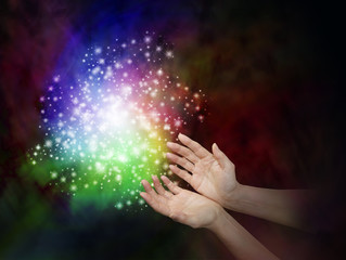 Wall Mural - magic dust - female hands reaching towards a cloud of rainbow colored sparkles on a dark background 