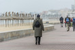 © HBpictures - Adult people walking on promenade at spanish coastline. Senior women and men on a beach in winter, cloudy sky