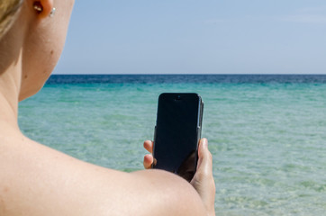 Youg girl reading mail and text message on the beach with her smartphone