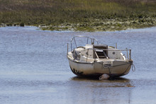  A Single Sailing Boat In An Estuary At Low Tide, Beached On The Wet Sand Awaiting The Incoming Tide
