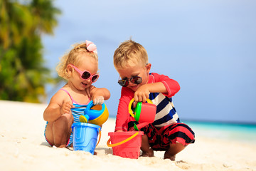 little boy and toddler girl play with sand on tropical beach