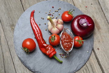 Wall Mural - Ketchup chili in a glass gravy boat and its ingredients on a bla