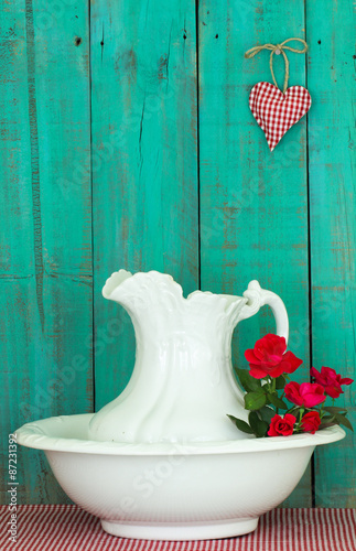 Fotografie, Obraz Antique water pitcher and basin with red roses by rustic green background