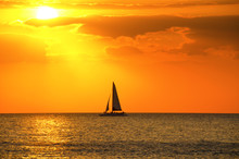 Beautiful Gold And Orange Sunset With A Sailboat Sailing Through The Beam Of Sunlight
