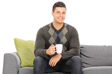 Poster - Young man holding a cup of coffee seated on sofa