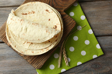 Wall Mural - Stack of homemade whole wheat flour tortilla on cutting board, on wooden table background