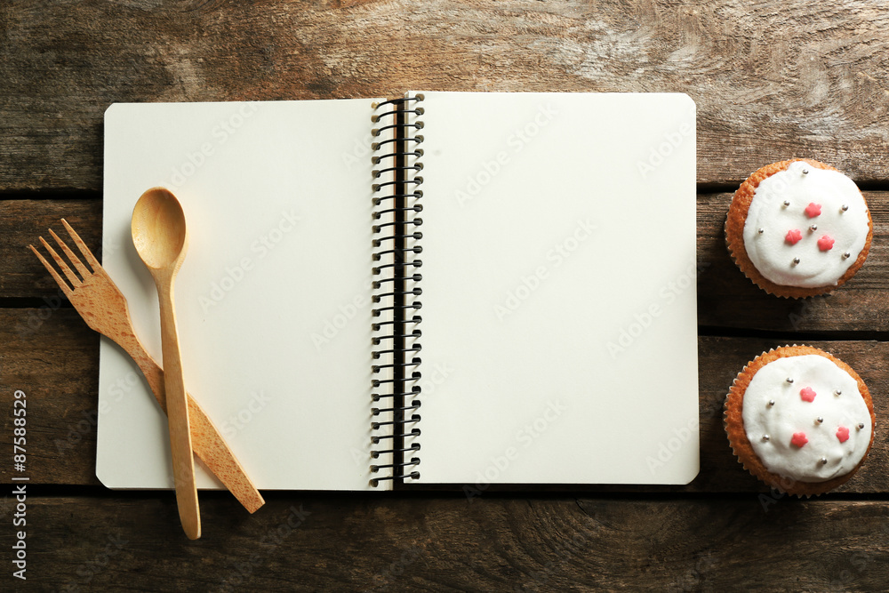 Open recipe book and tasty bakery on wooden background
