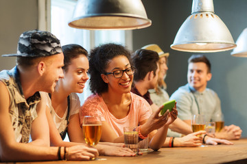 Wall Mural - happy friends with smartphone and drinks at bar