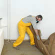 © sima - Adult worker with protective mask removing old carpet in room
