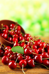 Fototapete - Pile of fresh cherries in bowl on wooden table on green blurred background