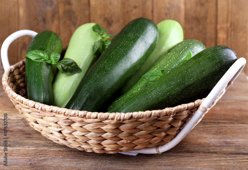 Fresh zucchini with squash and basil in wicker basket on wooden background