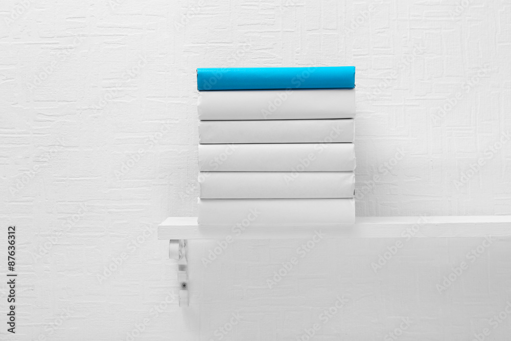 Blank books and one blue on shelf on white wallpaper background