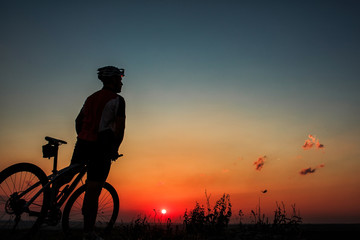 Silhouette of a biker and bicycle on sky background.